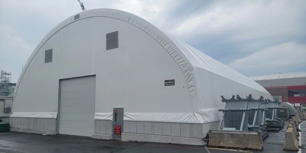 Large white industrial tent structure with a closed garage door under a cloudy sky.