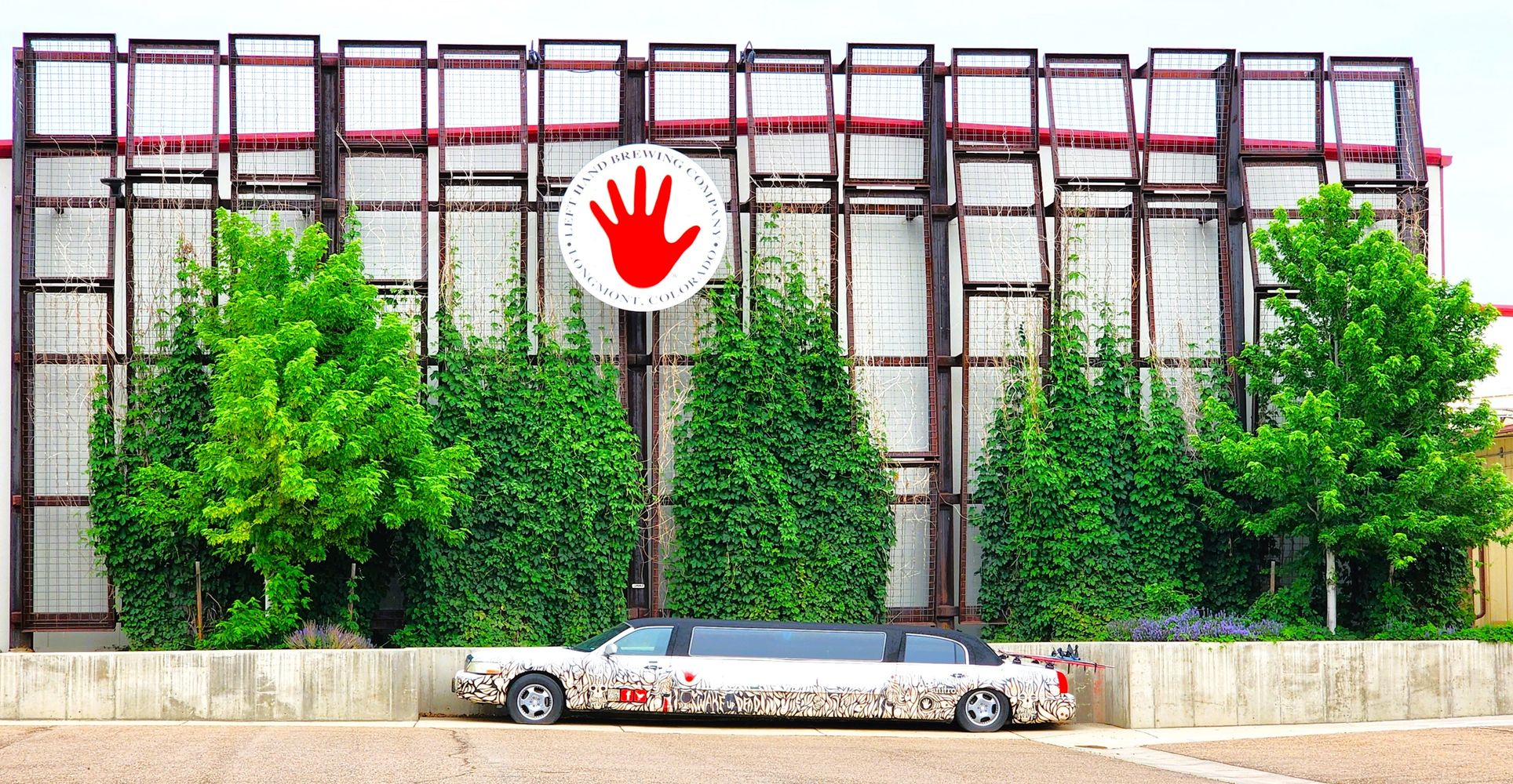 A uniquely decorated limousine parked in front of a green, vine-covered building.