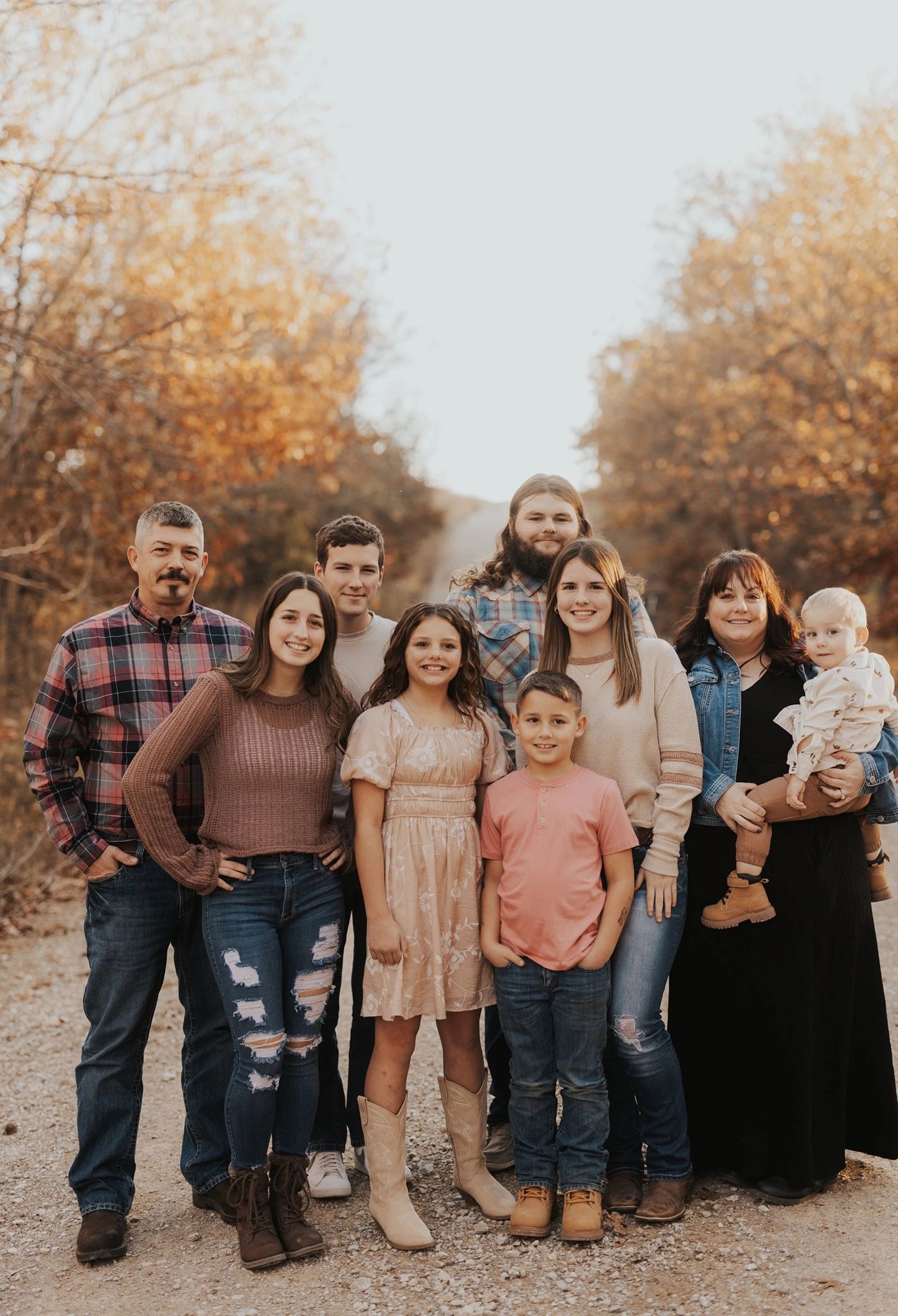 A happy family of nine posing outdoors in autumn with warm smiles.