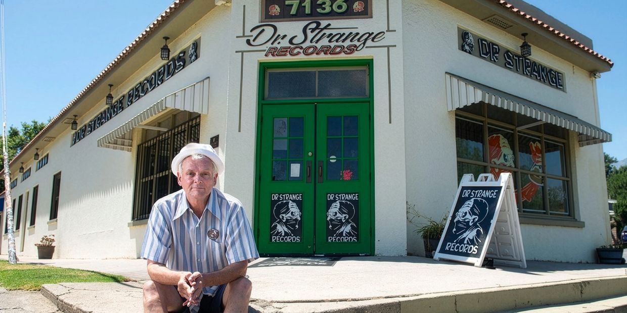 Man sitting outside Dr. Strange Records store with green doors.