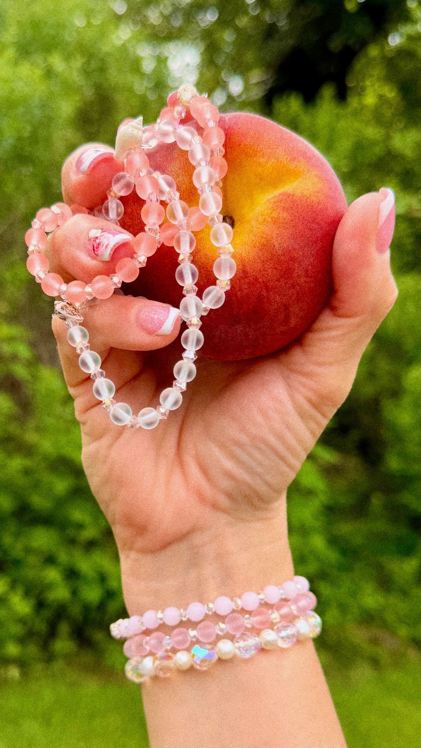 Hand holding a peach with pink beaded bracelets.