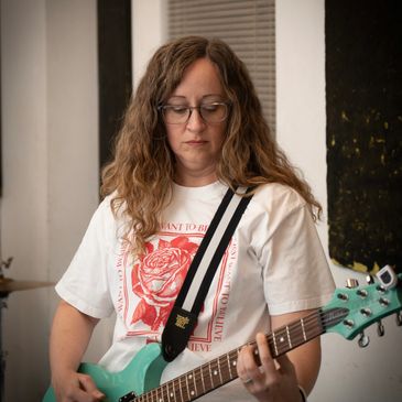 Woman playing a mint green electric guitar indoors.