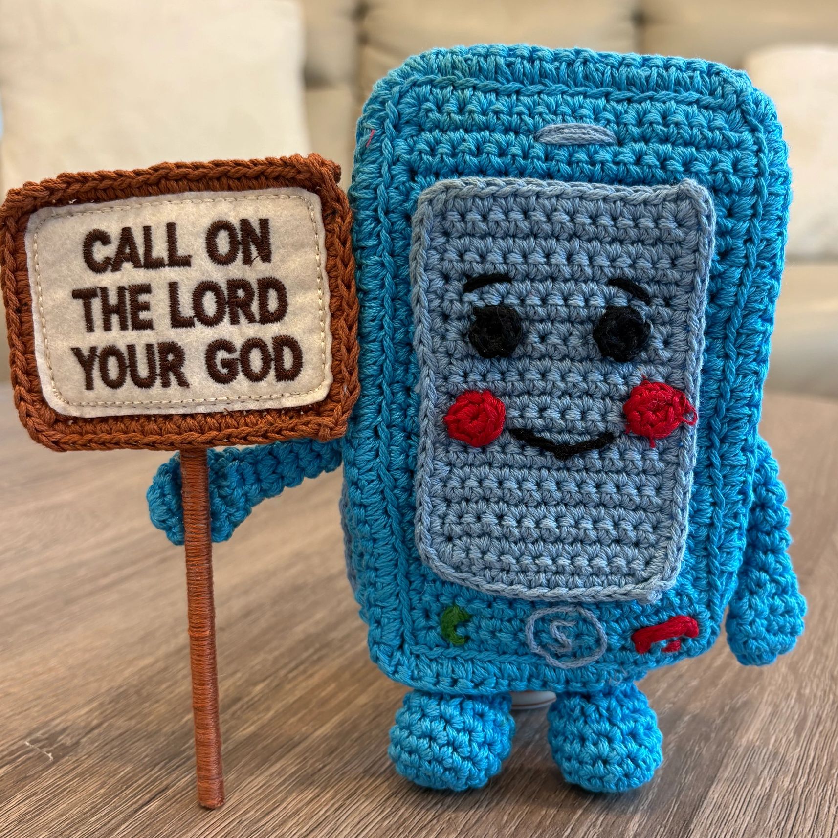Crocheted phone holding a sign with a religious message.
