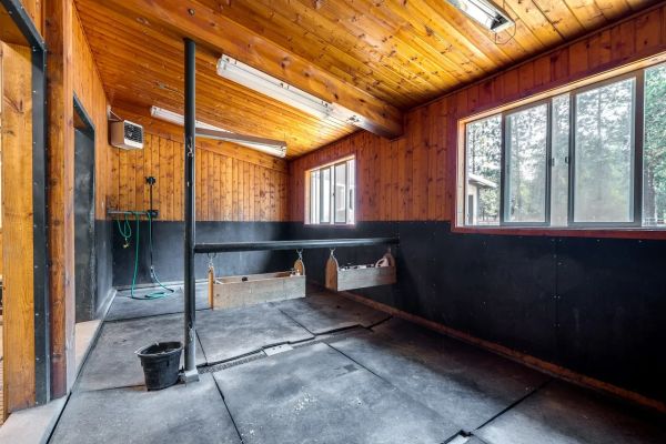 Interior of a rustic wooden stable with feeding troughs and large windows.