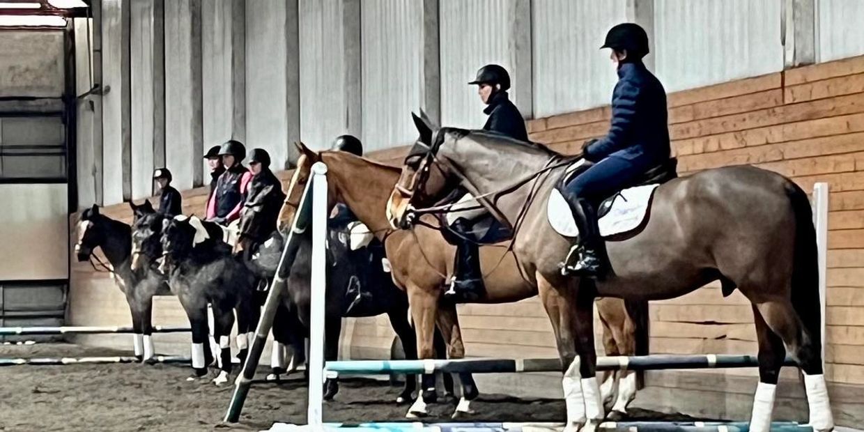 Riders on horses lined up indoors, ready for training or competition.