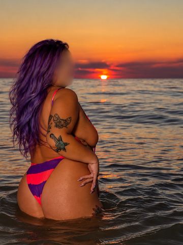Person with purple hair in the ocean at sunset.