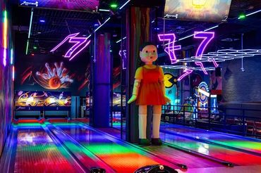 Bowling alley with colorful lights and a large doll figure.