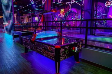 Vibrant neon-lit air hockey table in a colorful arcade setting.