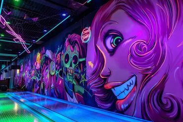 Vibrant neon graffiti art lines a bowling alley wall, creating a lively atmosphere.