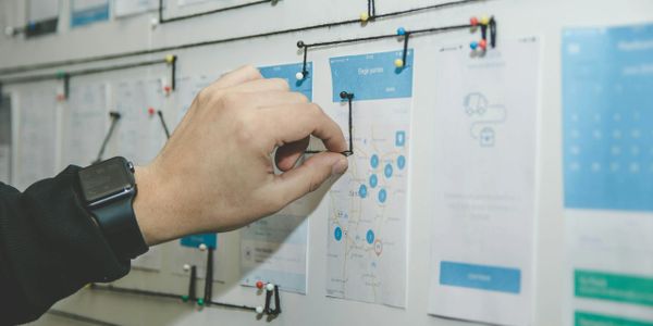 Hand adjusting a black wire on a map pinned to a board.