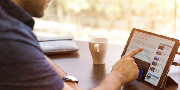 Person using a tablet to read news or articles at a table.