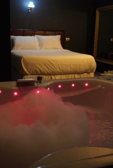 Cozy bedroom with a lit jacuzzi tub filled with bubbles and red lights.