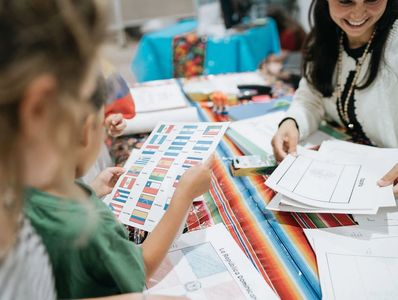A smiling volunteer helping students with a coloring activity at an event.