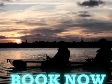 Two people in a clear kayak at sunset with the words "book now" on it in blue. 