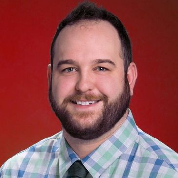 Smiling man in a plaid shirt and tie against a red background.