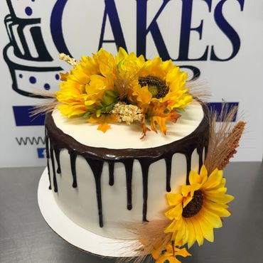 Elegant white cake with chocolate drip and sunflower decorations.