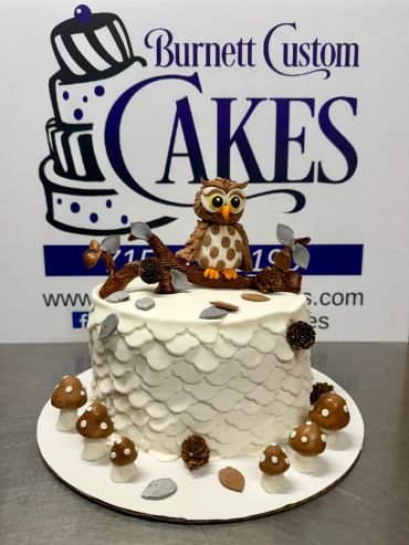 A white cake with an owl topper and autumn-themed decorations.