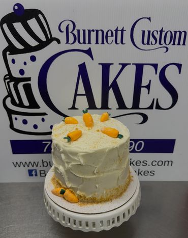 A white frosted cake decorated with small carrots on a cake stand.