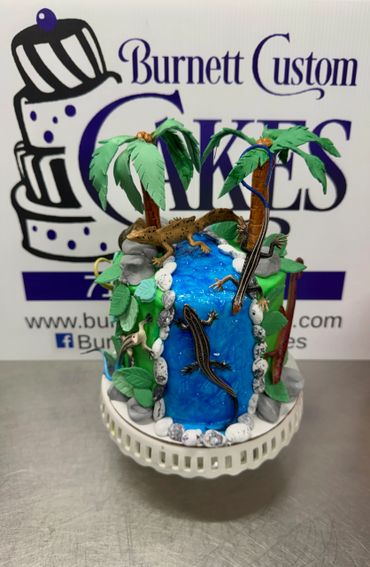 Tropical-themed cake with palm trees, lizards, and a waterfall design.