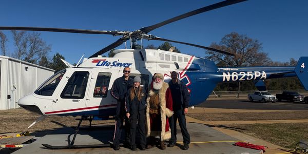 Santa Claus poses with three emergency medical personnel in front of a Life Saver helicopter.