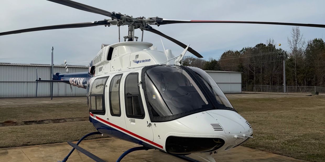 White and blue helicopter on a concrete pad with cloudy sky.