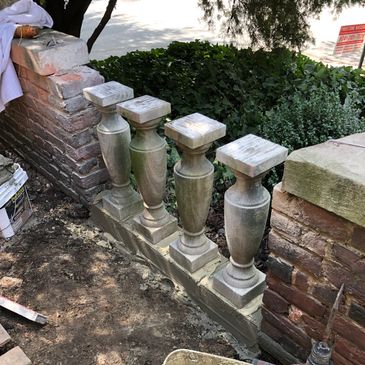 Four stone balusters being installed on a low wall with mortar and tools.