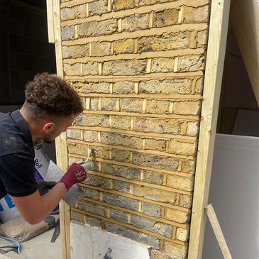 A man is applying mortar to a brick wall using a trowel.