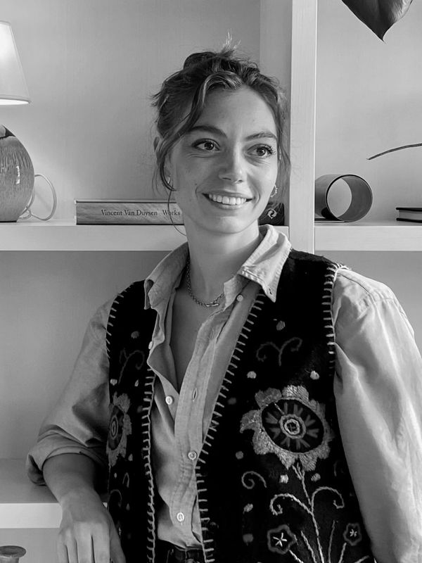 Smiling woman leaning on a white shelf with decorative items.