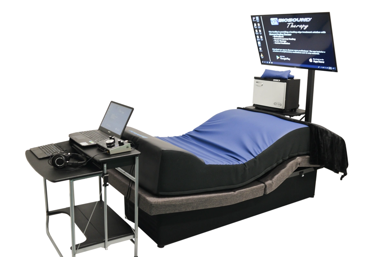 Advanced therapy bed setup with laptop, headphones, and monitor.