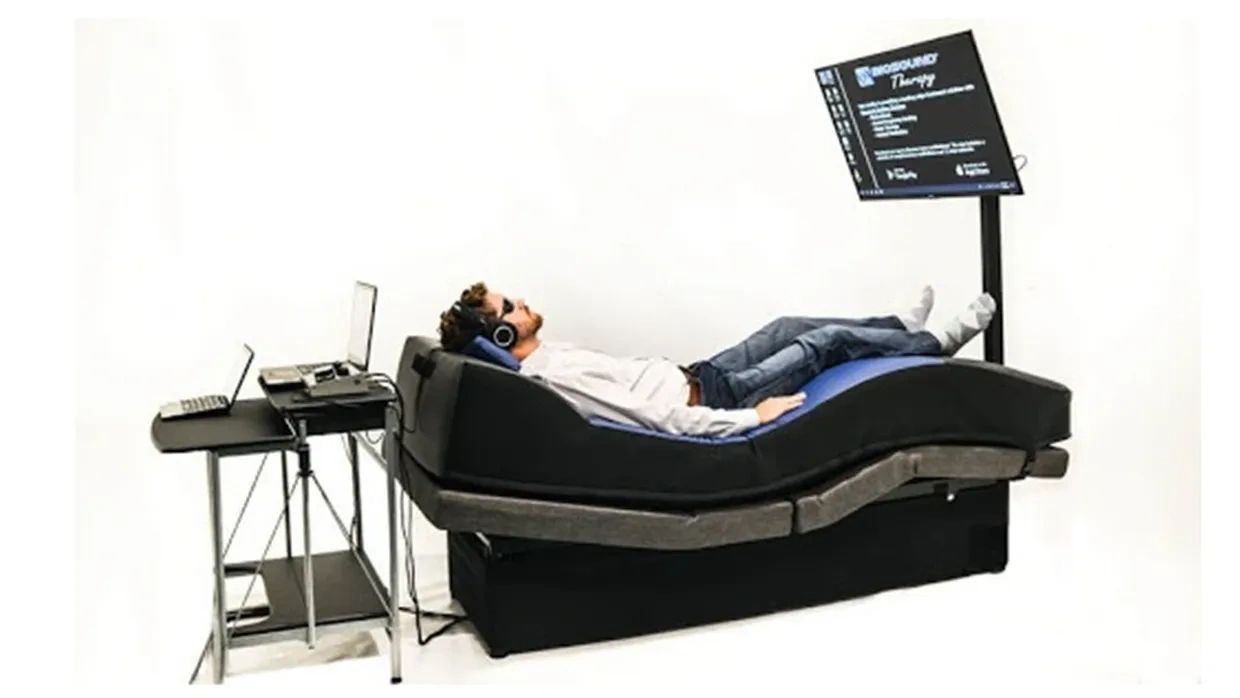 Man lying on a therapeutic bed with headphones and a screen nearby.