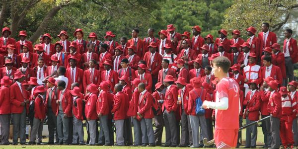 Group of students in red uniforms standing outdoors with a soccer player in foreground.