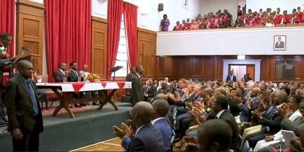 A formal event with an audience applauding a speaker in a wood-paneled room.