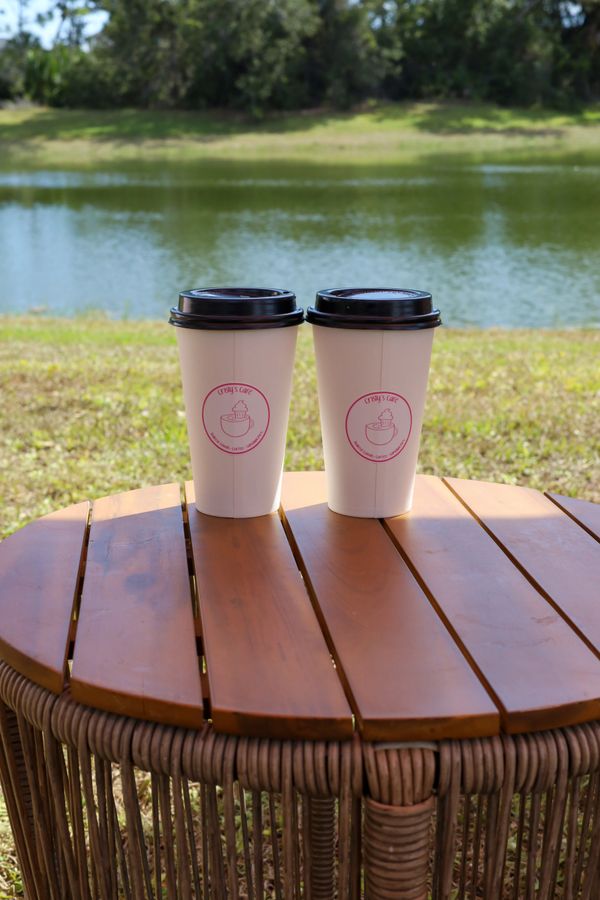 Two coffee cups on a wooden table by a lakeside under sunlight.