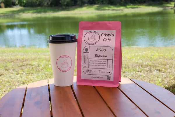 Coffee cup and espresso bag from Cristy's Café on a wooden table by a lake.