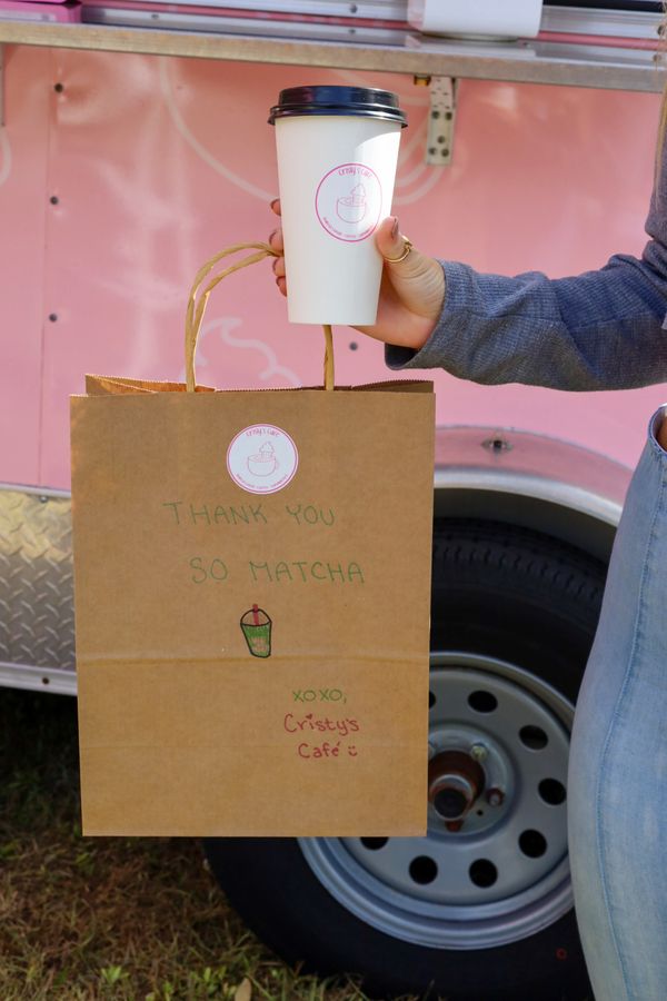 Person holding a coffee cup and a brown paper bag with a thank you note from Cristy's Café.