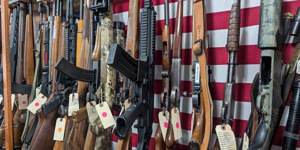 A collection of rifles and shotguns displayed against an American flag.