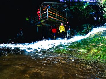 People stand near a wooden structure by a flowing river at night.