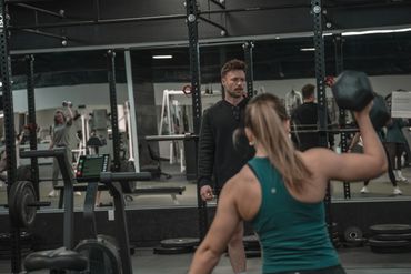 A woman lifting dumbbells with a trainer observing in a gym.