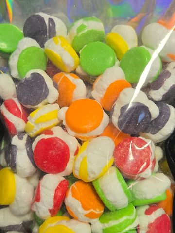 Colorful round candy pieces coated in white icing inside a clear bag.