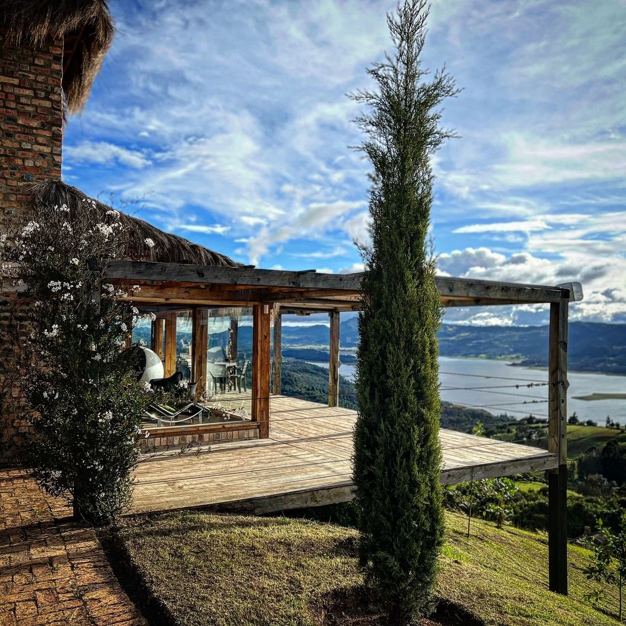 Scenic wooden terrace overlooking a lake and mountains under a blue sky.