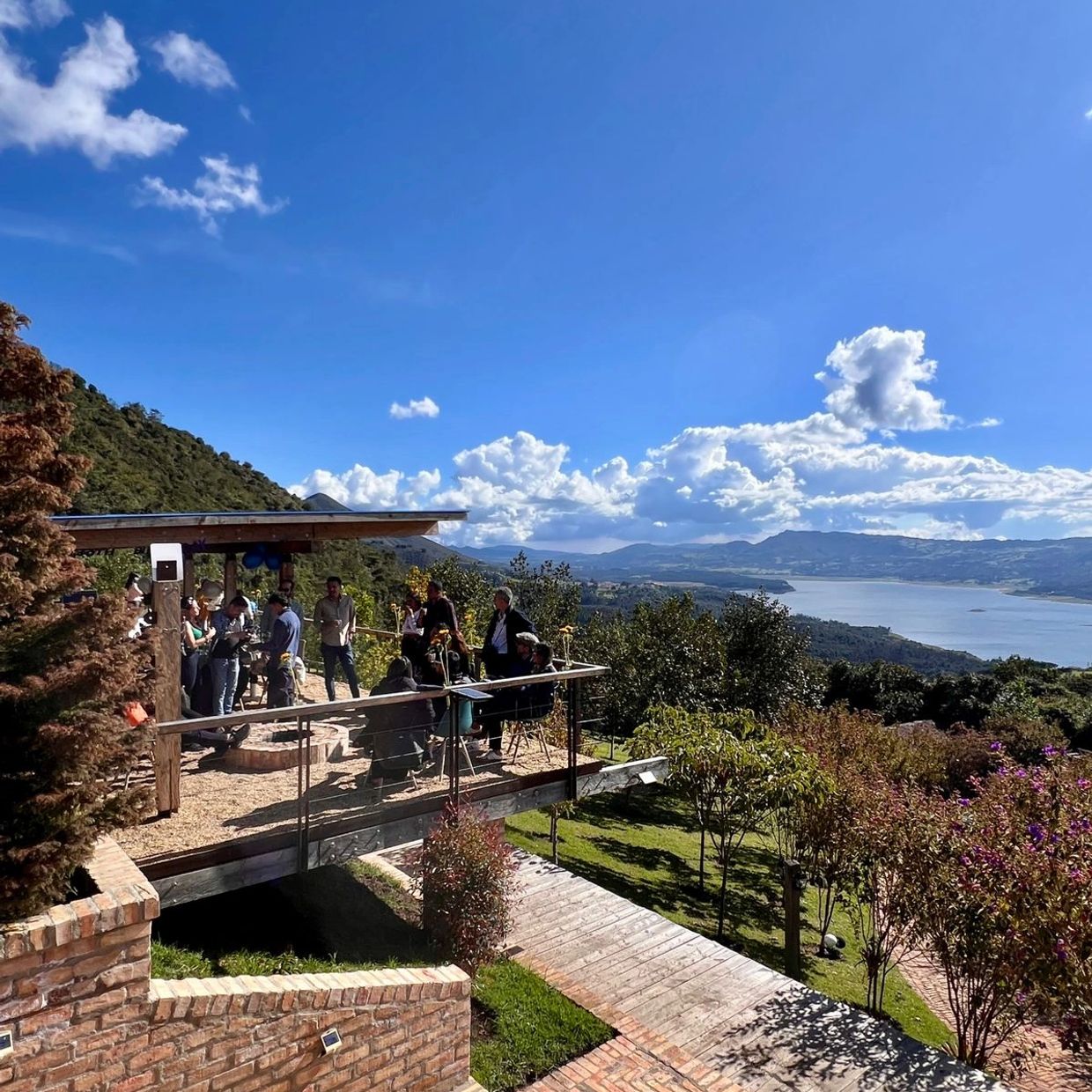Group of people socializing on a wooden deck with scenic lake and mountain views.