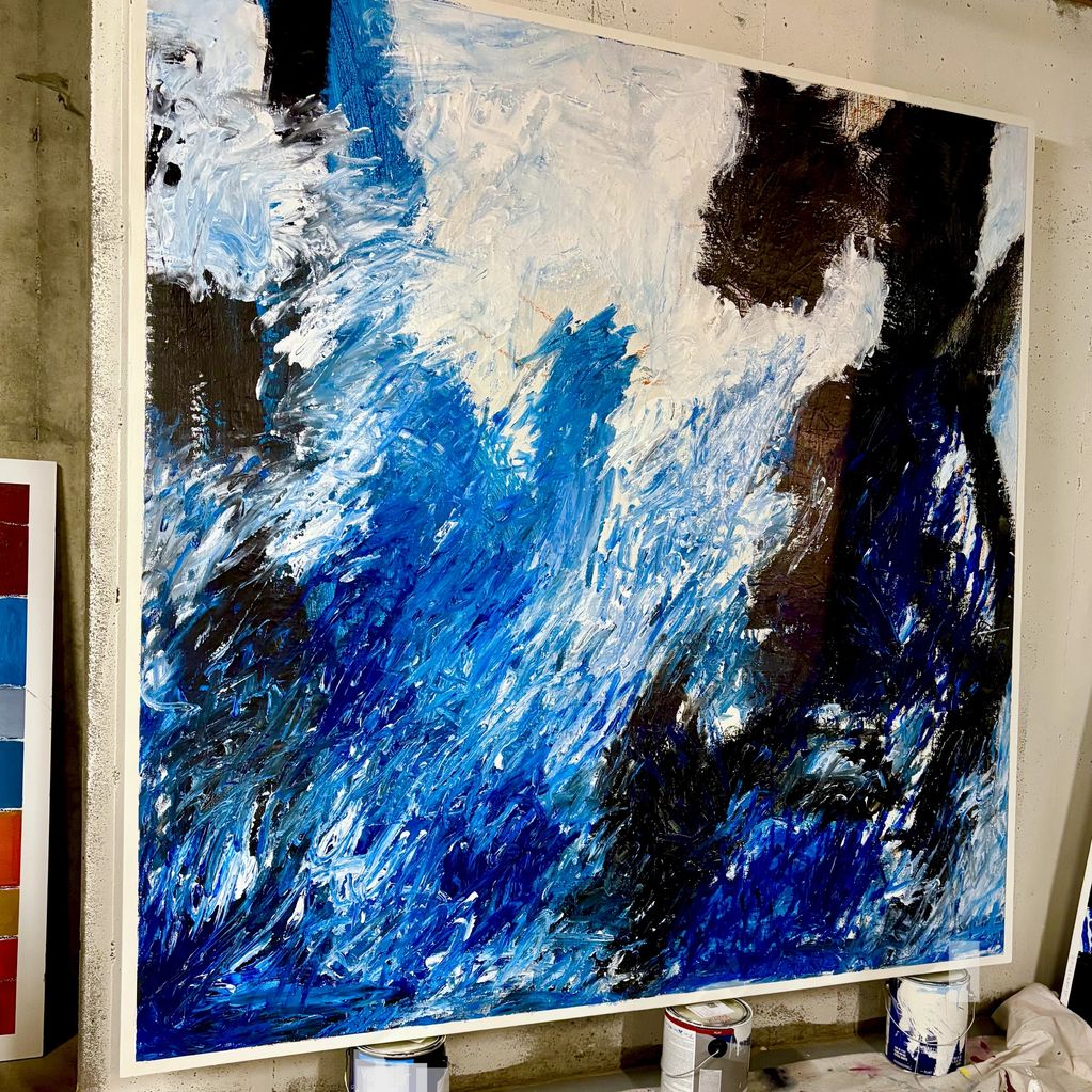 Abstract painting with dynamic blue, white, and black brushstrokes on a large canvas.