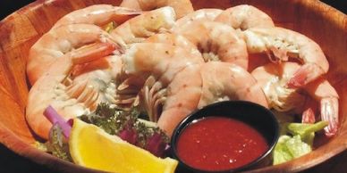 A bowl of cooked shrimp with cocktail sauce and lemon wedge.