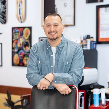 Smiling man leaning on a chair in a barbershop setting.