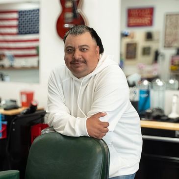 Man in white hoodie leaning on barber chair in a barbershop.