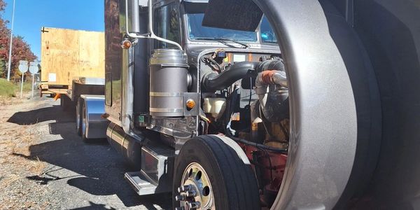 This image shows a commercial truck receiving roadside repairs on a sunny day. 