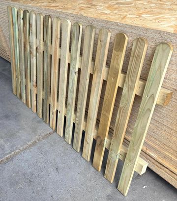 Wooden picket fence panels leaning against a wooden stack.