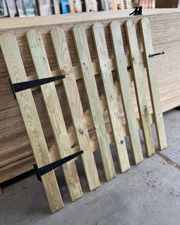 Wooden fence panel with metal brackets leaning against plywood sheets.