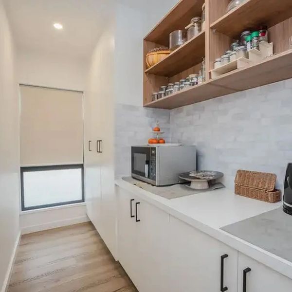 Modern kitchen corner with white cabinets, microwave, and wooden shelves.
