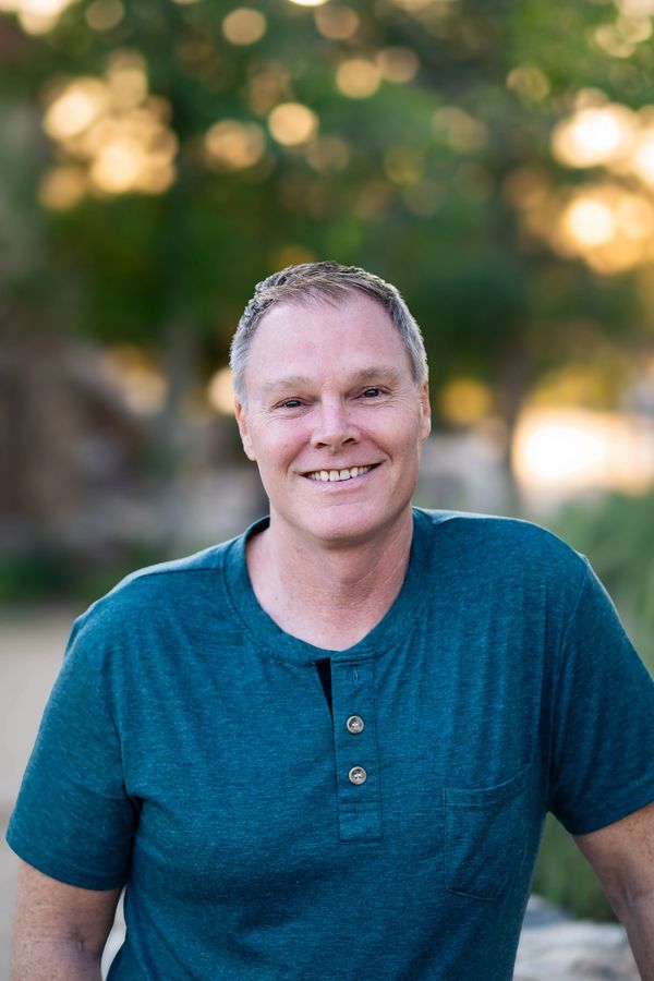 Smiling man in a teal shirt outdoors.